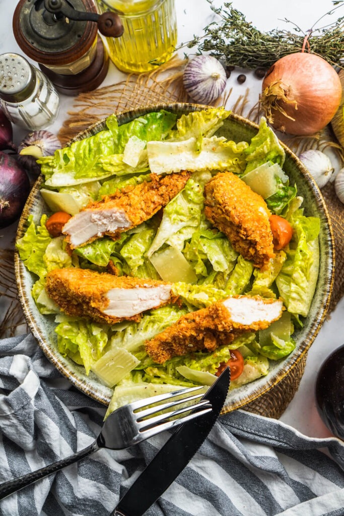 Ein großes Teller voll von Romana Salat und aufgeschnittenen, knusprigen Hähnchenstreifen.