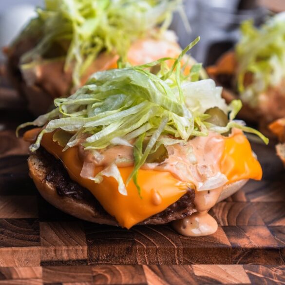 Big Mac Brötchen auf einem Holzbrett mit Salat oben drauf