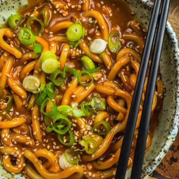 Eine Schüssel mit dicken Udon Nudeln, cremiger Erdnussbutter Soße, Sesam und Frühlingszwiebeln sind oben drauf, Nahaufnahme