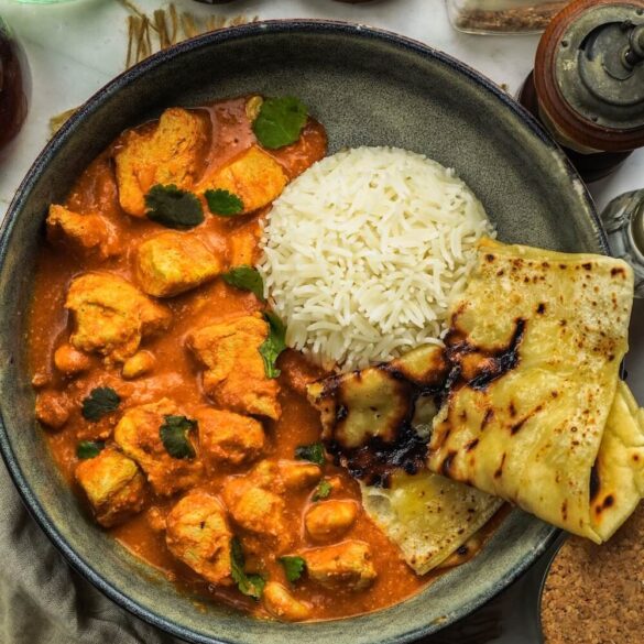 Cashew Butter Chicken in cremiger Tomaten-Cashew-Sauce, serviert mit frisch gebackenem Käse Knoblauch Naan auf einem Teller