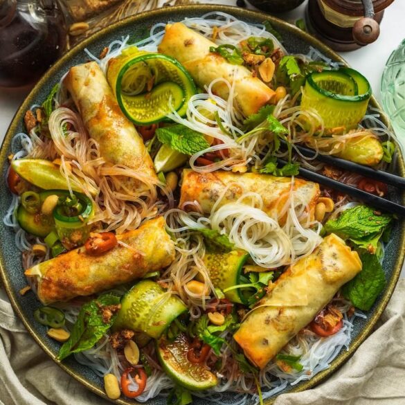 Ein Teller voller Glasnudel Salat, mit vielen verschiedenen Toppings und goldbraunen Frühlingsrollen