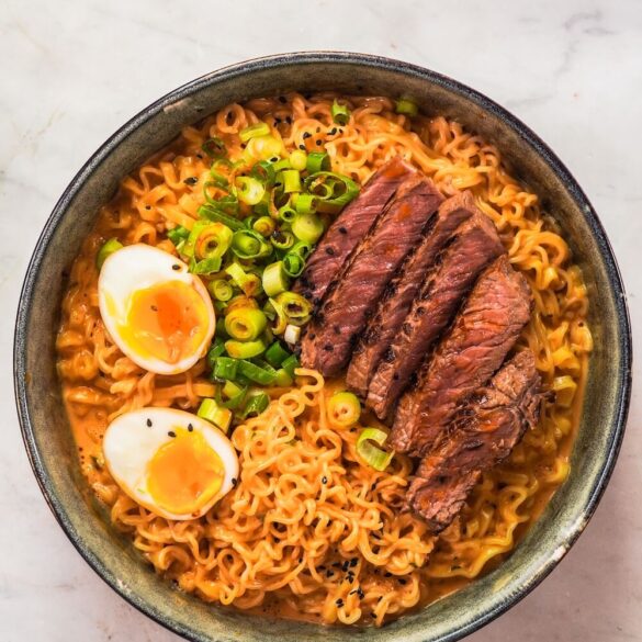 Eine Schüssel voll Steak Buldak Ramen mit Nudeln, Eiern, Steakstreifen und Frühlingszwiebeln