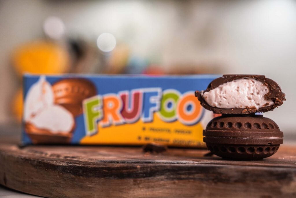 Zwei Schokoladen Frufoo Ufos aufeinander, der obere halbiert sodass man die Füllung sieht. Im Hintergrund unscharf ein Remake der Originalen Verpackung.
